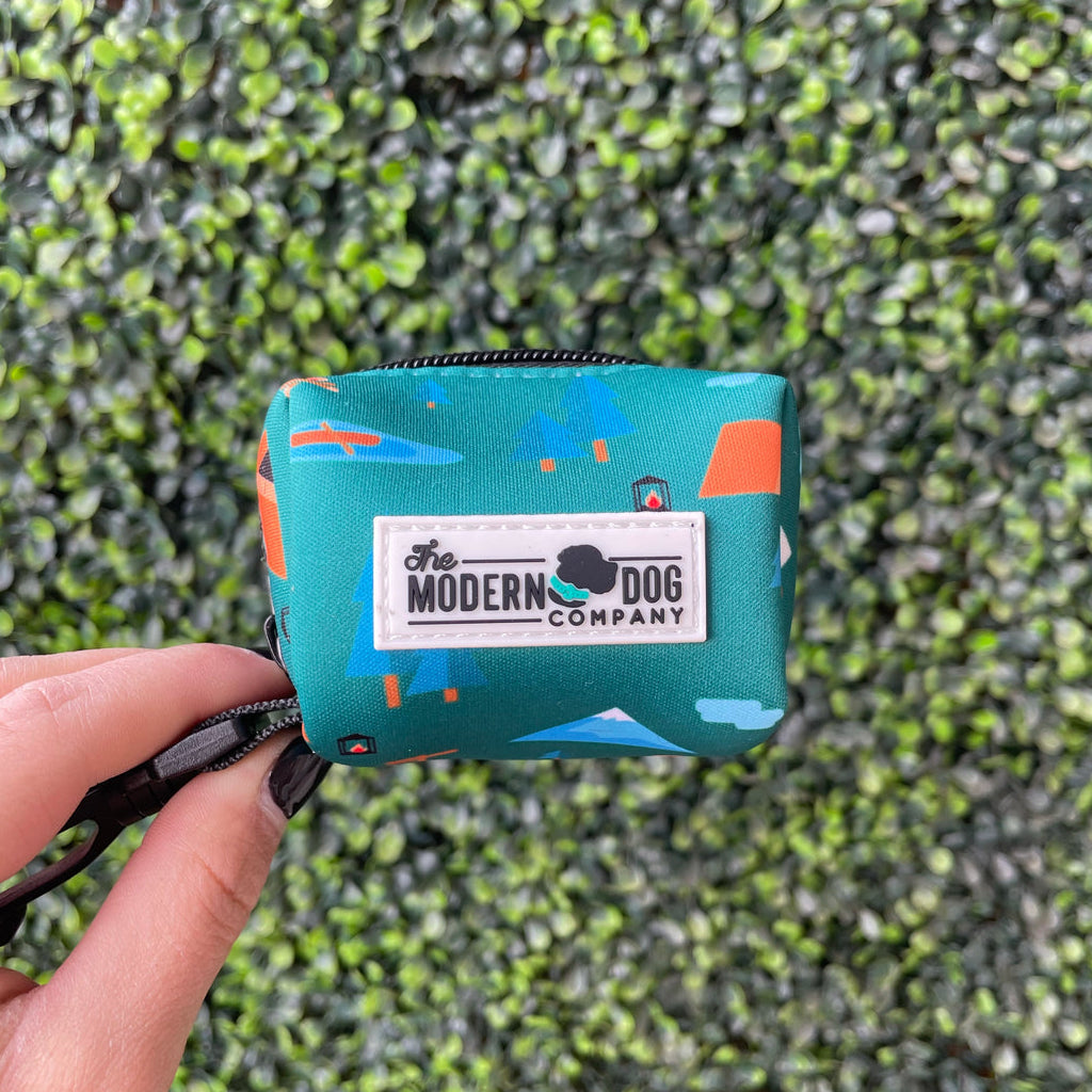 Teal poop bag pouch with 'The Modern Dog Company' logo held by a hand against a green grass background