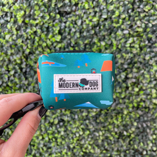 Teal poop bag pouch with 'The Modern Dog Company' logo held by a hand against a green grass background