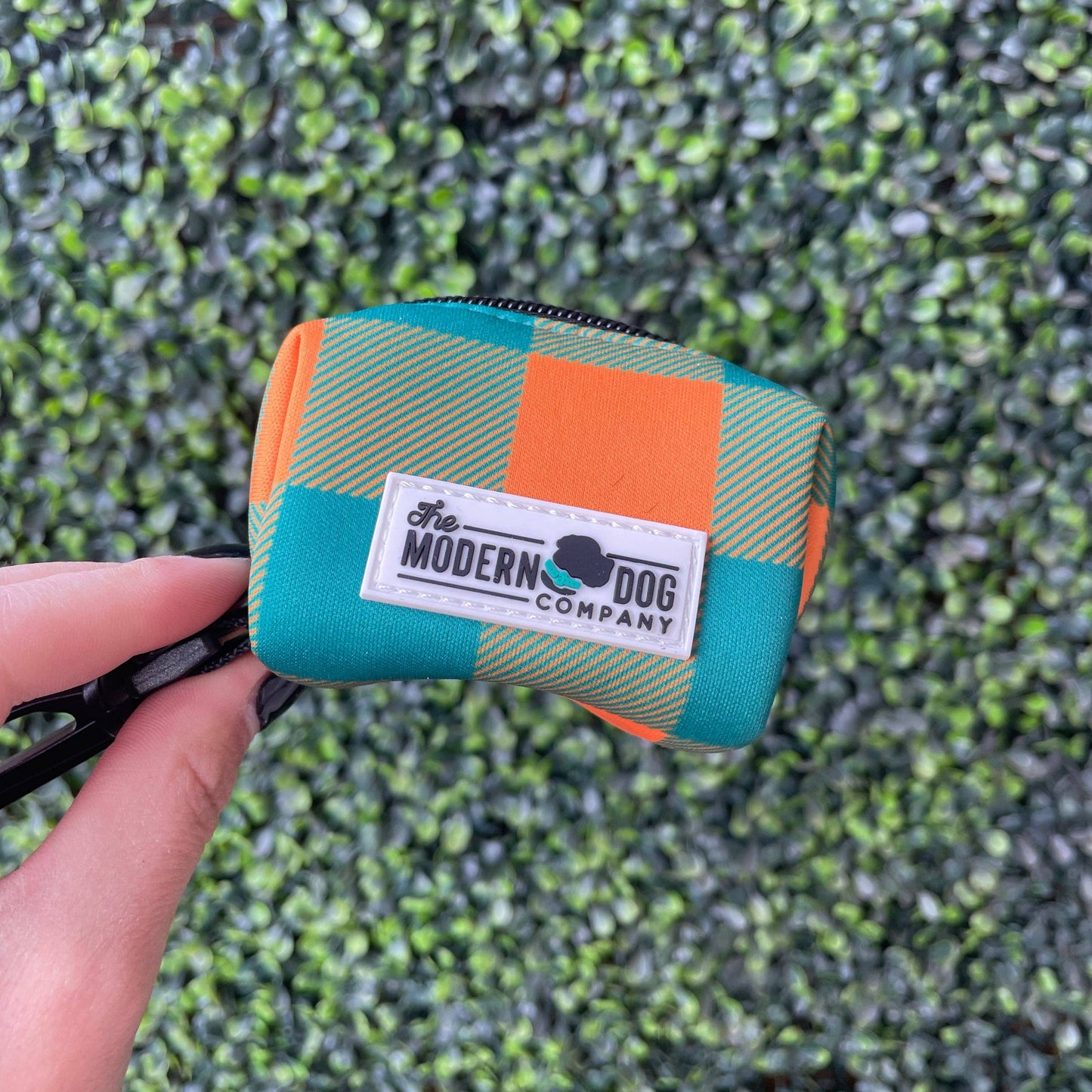 Small poop bag pouch with a checkered pattern held by a hand on a grassy background